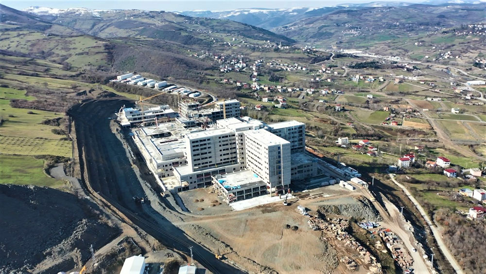 Samsun'da Sağlık Bakanlığı'nın öz kaynaklarıyla yapılan 900 yataklı Samsun Şehir Hastanesi’nin kaba inşaatının yüzde 95’i, genel durumunun ise yüzde 46'sı tamamlandı. 'Örnek hasta odası' ortaya çıkan hastanede 5 yıldızlı otel konforu olacak.  HASTA VE YAKINLARINA RAHAT ODA Samsun'un Canik ilçesi yamaçlarına yapılan dev hastane, Karadeniz'i Anadolu'ya bağlayan çevre yolundan geçen herkesin dikkatini çekiyor. İnşaatı hızla devam eden Samsun Şehir Hastanesi'nde fiziki gerçekleşme yüzde 95, genel tamamlanma oranı ise yüzde 46 düzeyinde. Çalışmalar devam ederken örnek bir hasta odası da yapıldı. Hastanenin örnek odası ilk kez görüntülendi. Otel konforunda olan, birçok imkanı bulunduran oda; hasta ve yakınlarına rahat bir ortam sunmak için tasarlandı.  KASIM 2023'TE HİZMETE GİRECEK Şehir Hastanesi Proje Koordinatörü Deniz Yıldız, “Hastanemiz ilerleme olarak yüzde 46 seviyesindedir. Yaz ayı başlarında artık cephelerimiz kapanacak ve Kasım 2023 itibarıyla inşallah Sağlık Bakanlığı ile birlikte hastaneye işletmeye almak istiyoruz. Bizim hastanemiz deprem sırasında toplanma alanı olarak kullanılabilir. Gayet büyük olan otopark alanımızla güven merkezi olacağını tahmin ediyoruz. Bu binalar yıkılmayacak şekilde hazırlanmıştır. Deprem izolatörlü binada ise asıl özellik deprem anında bile hem depremi oluştuğu şekilde hissetmemek hem de deprem sırasında elektrik, mekanik, doğalgaz, su gibi sistemlerin kesintiye uğramayıp devam etmesi sağlamak başlıca görevleridir” dedi.  SAĞLIK ÜSSÜ OLACAK Yapımı bittiğinde bir sağlık üssü haline gelecek hastane; genel tedavi üniteleri dışında onkoloji hastanesi, son teknoloji tetkik cihazlarıyla donatılmış bir nükleer tıp merkezi, kalp damar cerrahi ve göğüs merkezi, genetik hastalıkların tedavi sürecinin yönetileceği genetik hastalıklar merkezi, üreme yardımcı tedavi merkezi, organ ve doku nakli merkezi, inme merkezi, yanık merkezi, 40 ameliyathane ve 1 hibrit ameliyathaneyi bünyesinde bulunduracak.  İHA
